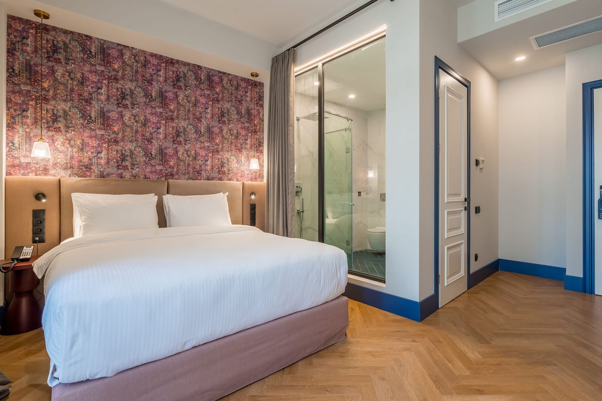 A modern hotel room with a large bed, a glass shower enclosure, and a patterned wall.