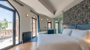Un dormitorio moderno con una cama grande, un baño con bañera independiente y vistas a un paisaje urbano a través de amplios ventanales.