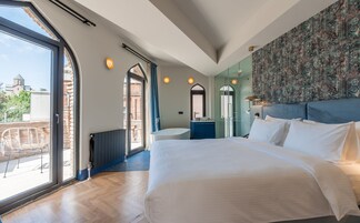 Un dormitorio moderno con una cama grande, un baño con bañera independiente y vistas a un paisaje urbano a través de amplios ventanales.