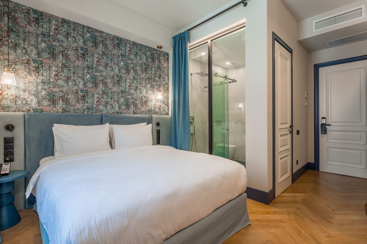 A hotel room with a large bed, a shower area, and a wardrobe.