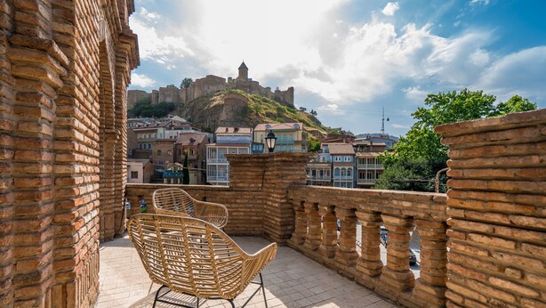 Un balcón con sillas de mimbre, un muro de ladrillo y vistas a un castillo histórico.