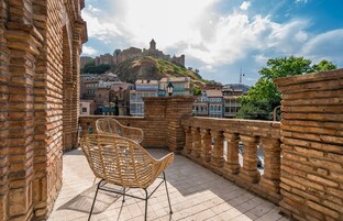 Un balcón con sillas de mimbre, un muro de ladrillo y vistas a un castillo histórico.