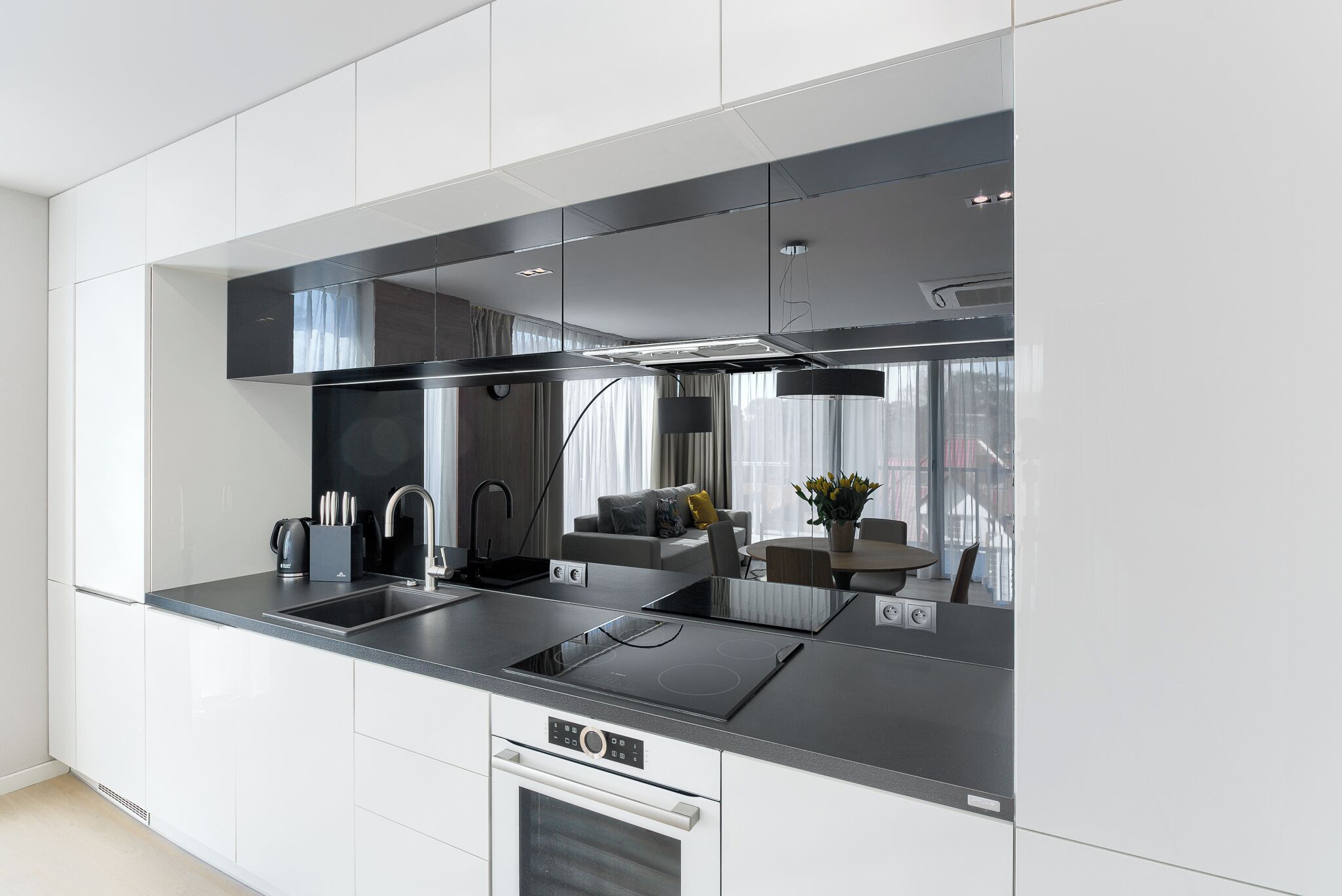 A modern kitchen with white cabinetry, black countertops, and stainless steel appliances.