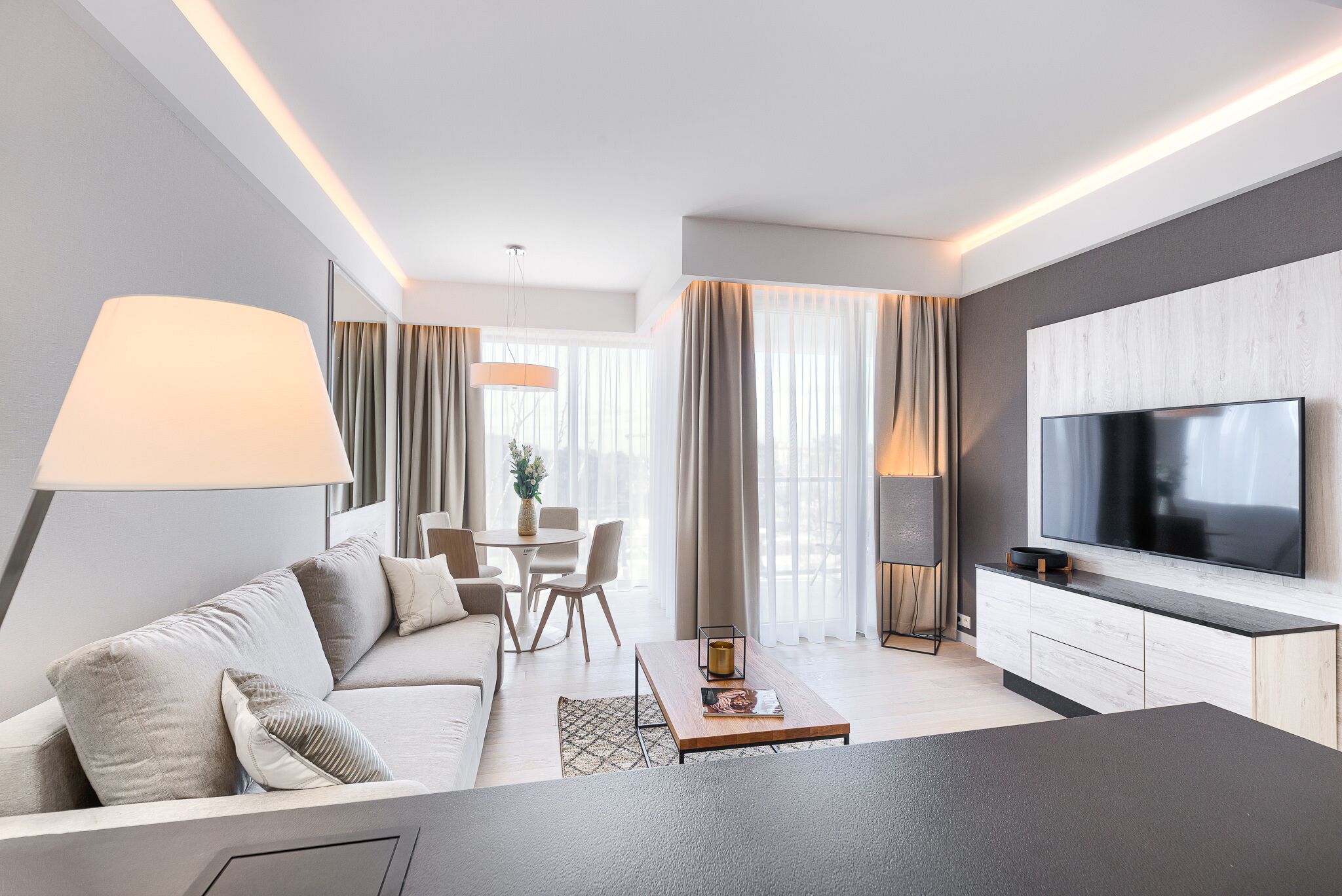 A modern living room with a sofa, coffee table, TV, and dining area.