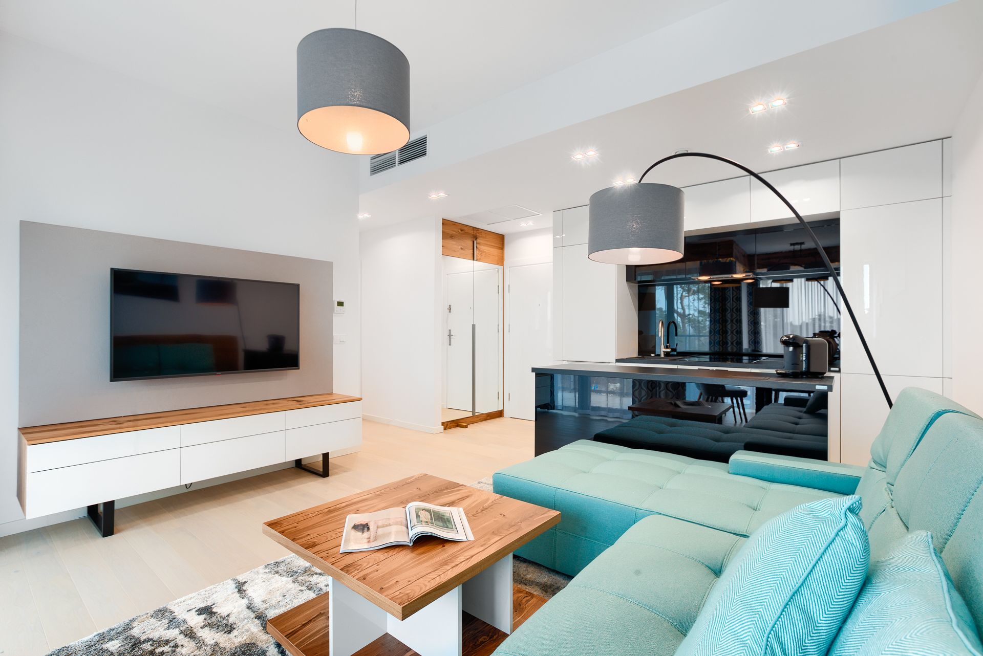 Ein modernes Wohnzimmer mit einem Flachbildfernseher, einem Holztisch und einem türkisfarbenen Sofa.