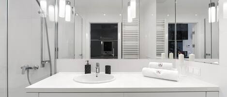 A modern bathroom with a white sink, a glass shower enclosure, and a large mirror.