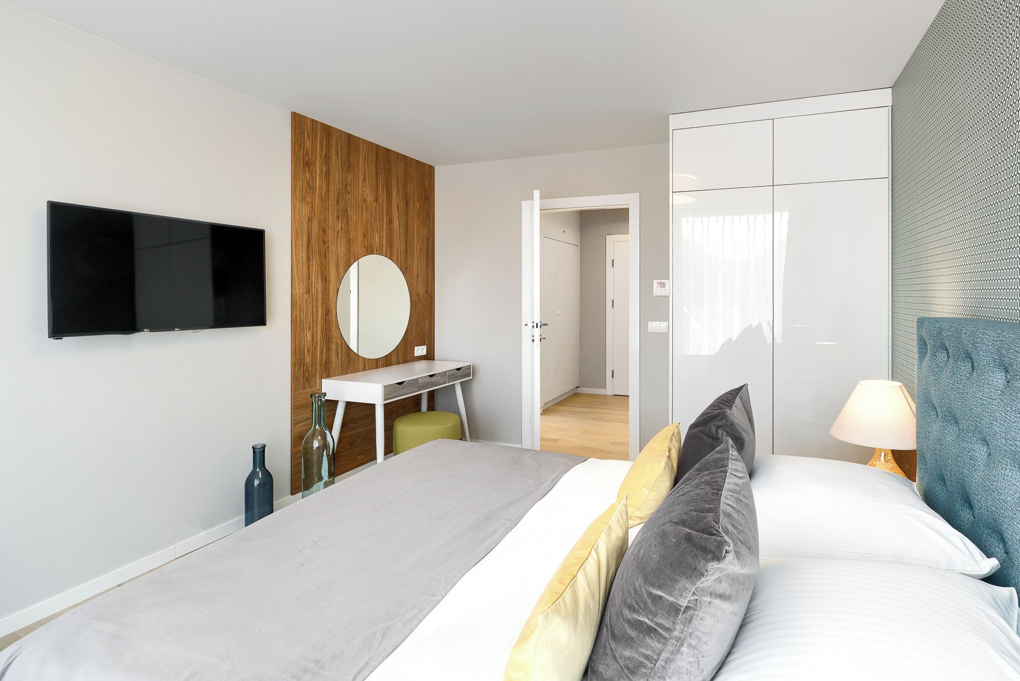 A modern hotel room with a bed, a desk, a TV, a mirror, and a wardrobe.
