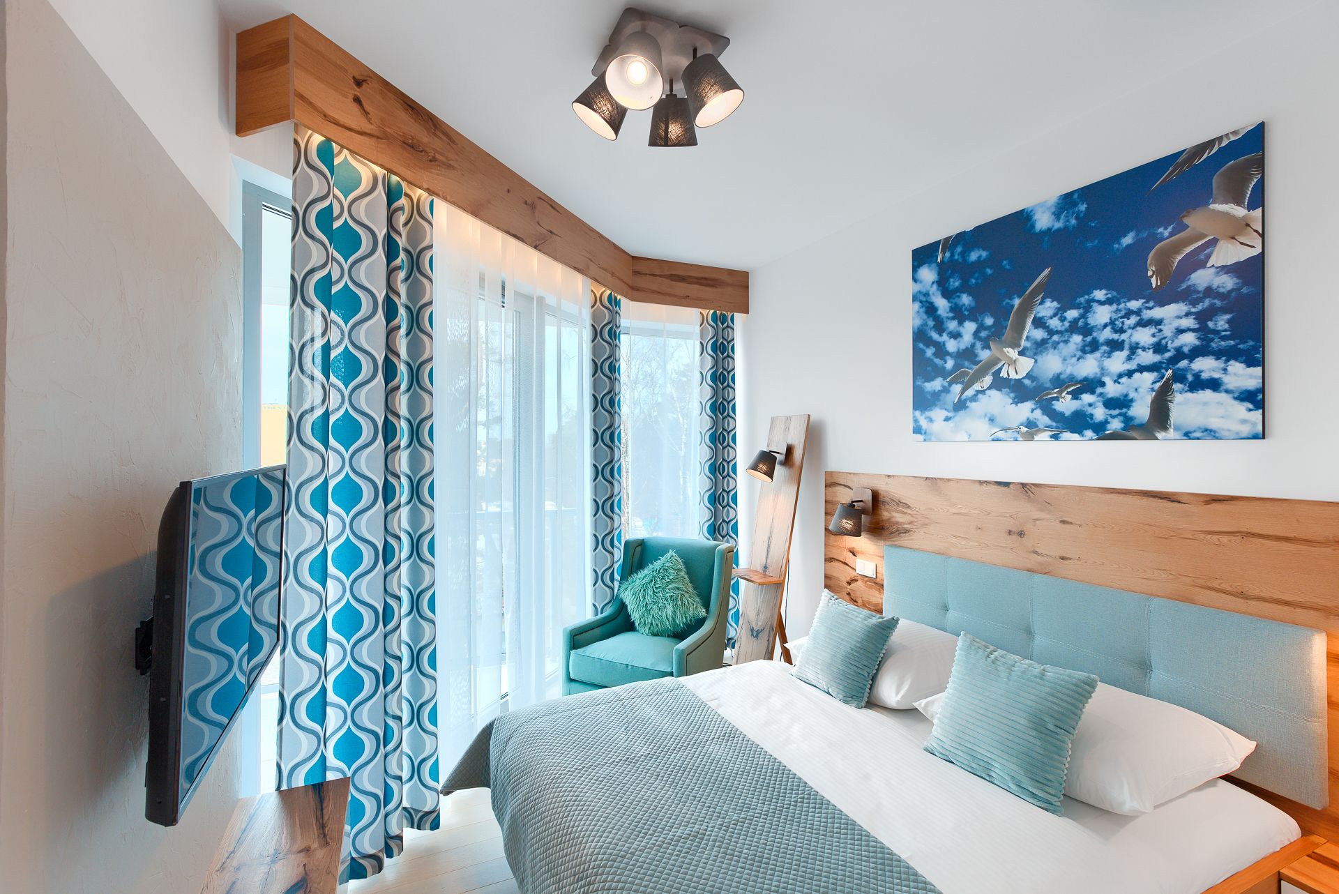 A bedroom with a bed, a chair, a TV, and a painting of birds.