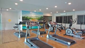 Et fitnesscenter med flere løbebånd, træningscykler og et muralmaleri af et landskab.