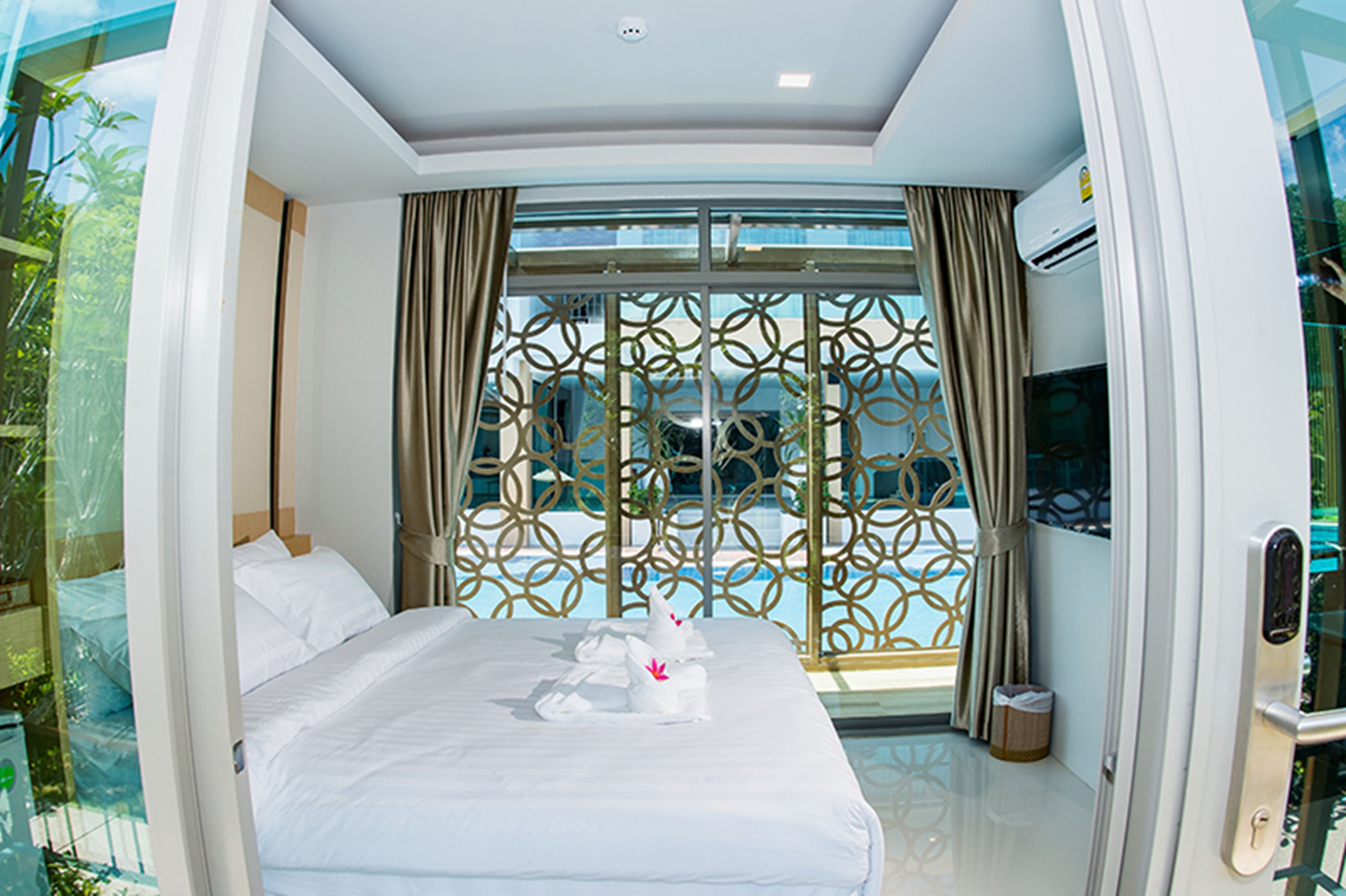 A hotel room with a bed, a TV, and a large window with a decorative screen.