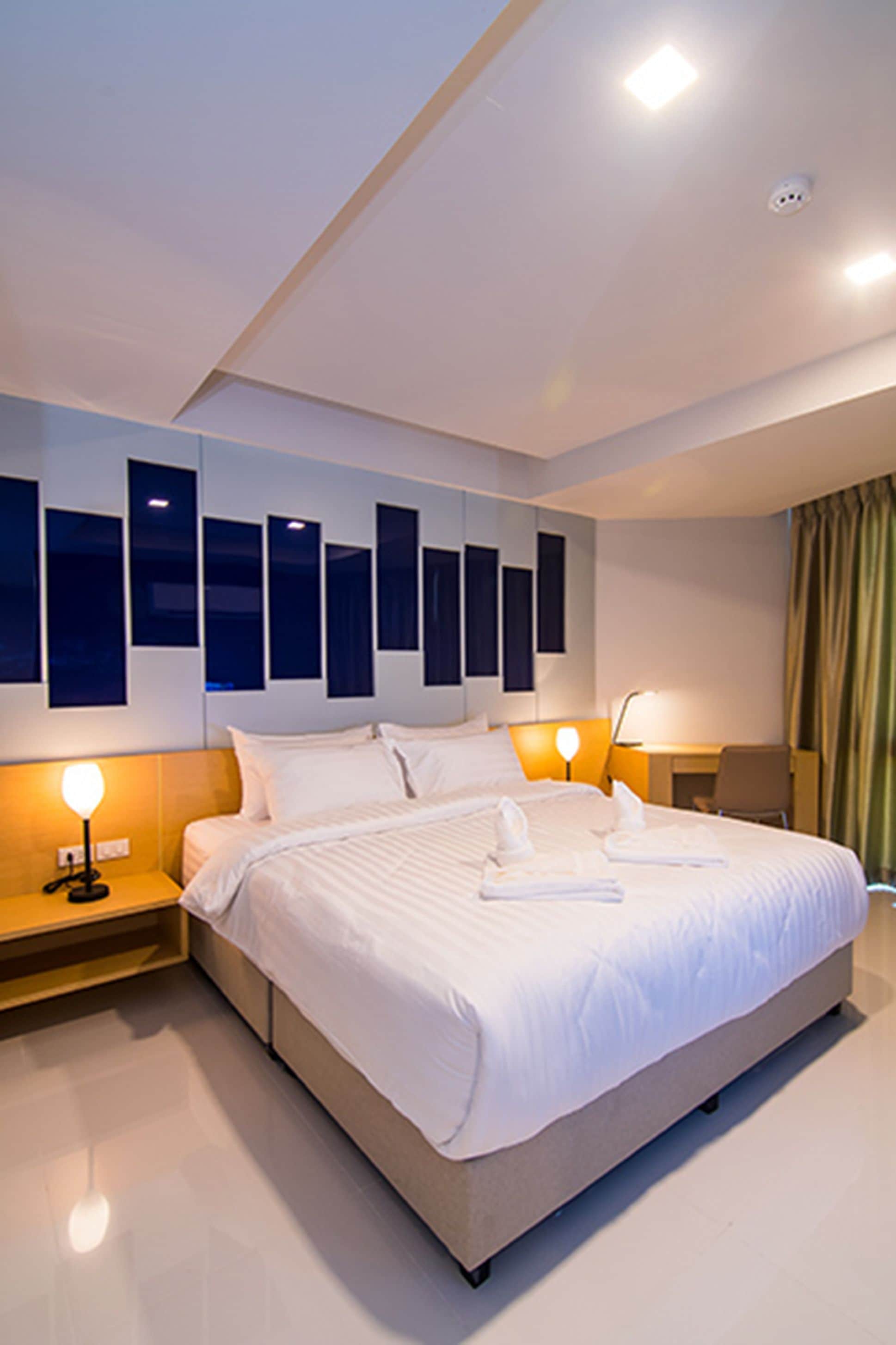 Una habitación de hotel moderna con una cama grande, mesitas de noche y una obra de arte colgada en la pared.