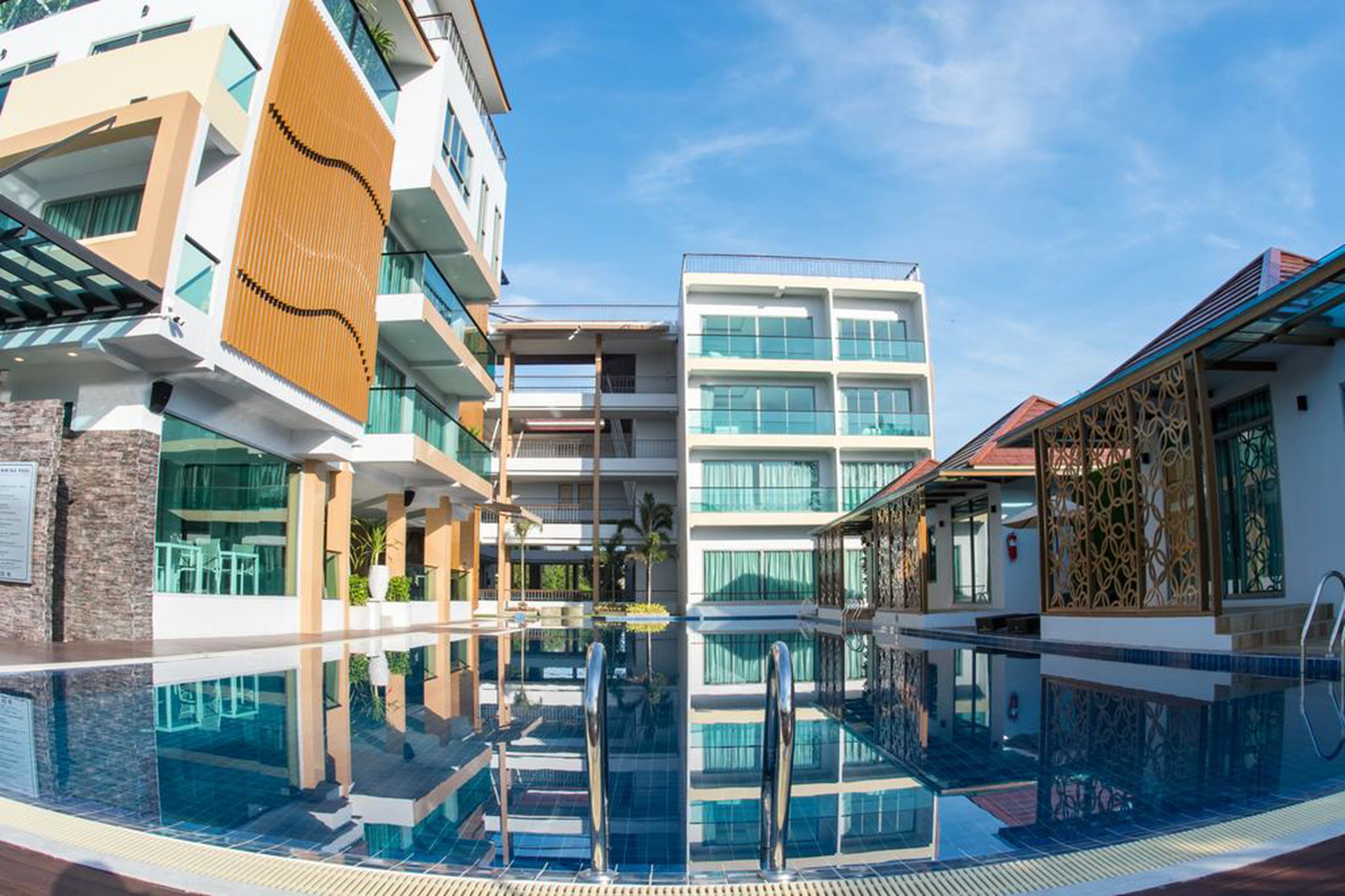 A modern hotel with a central pool, multiple balconies, and a clear sky.