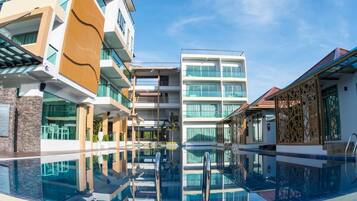 A modern hotel with a central pool, multiple balconies, and a clear sky.