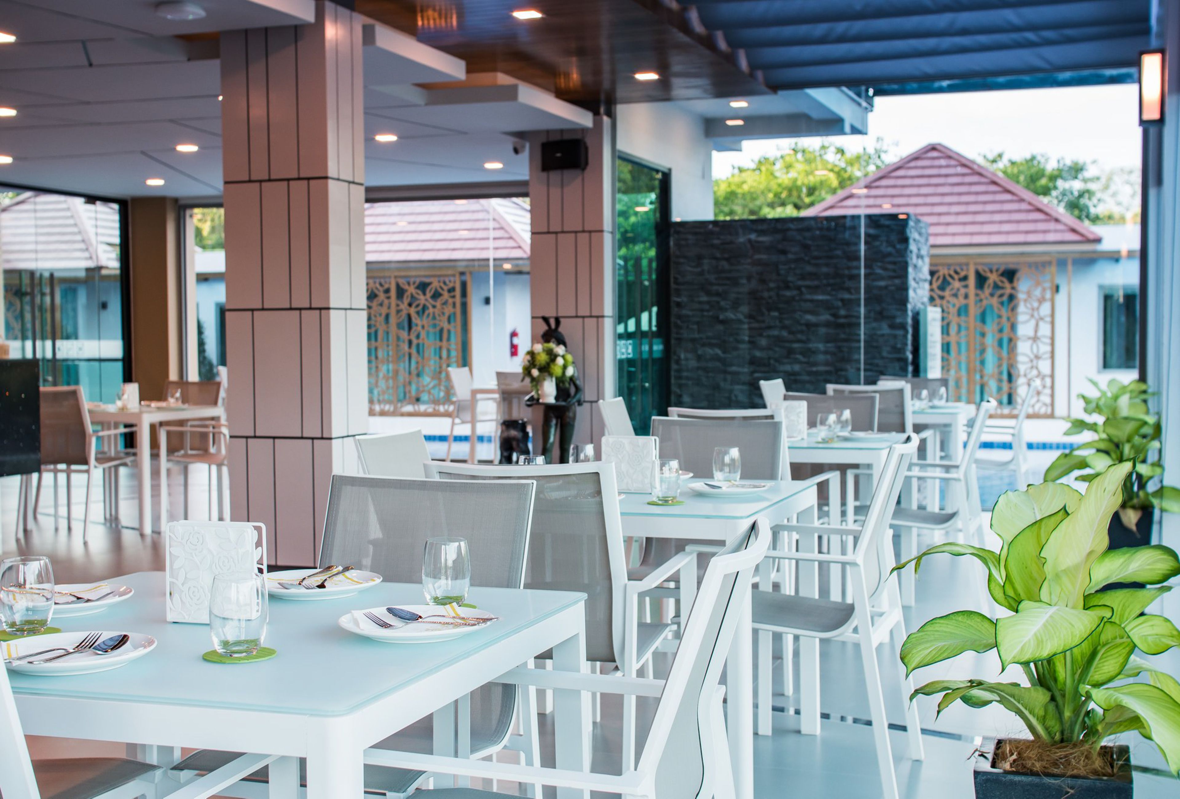 En restaurant med hvide borde og stole, en stenvæg og en potteplante.
