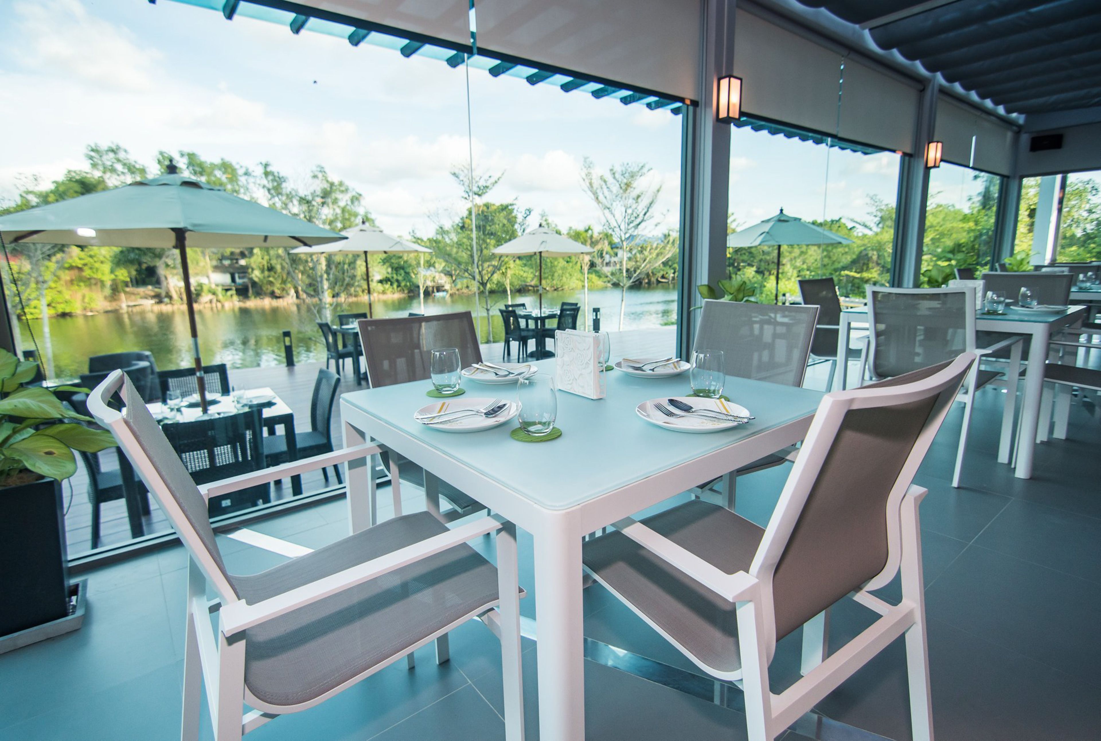 A restaurant with outdoor seating overlooking a body of water, featuring white tables and chairs, and umbrellas.