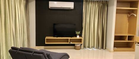 Una sala de estar moderna con un sofá, un televisor sobre un mueble de madera, aire acondicionado y un vestidor.