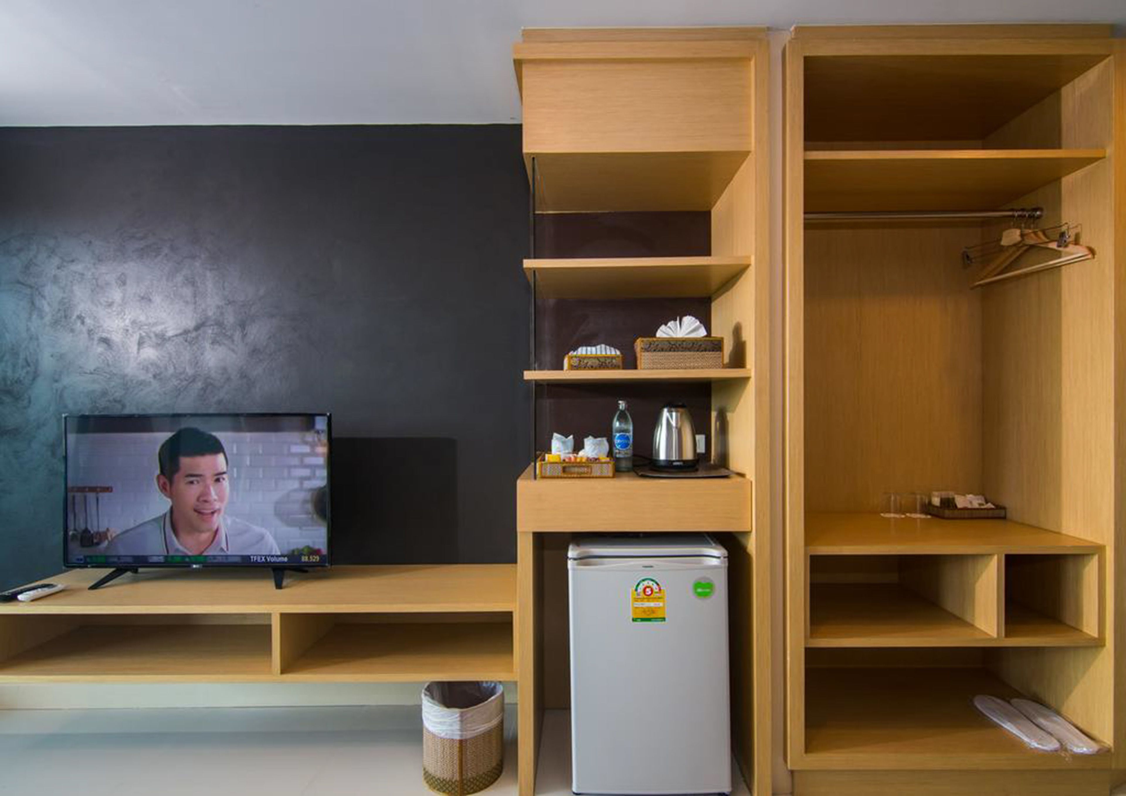 A compact living space with a television, a refrigerator, and wooden shelving units.