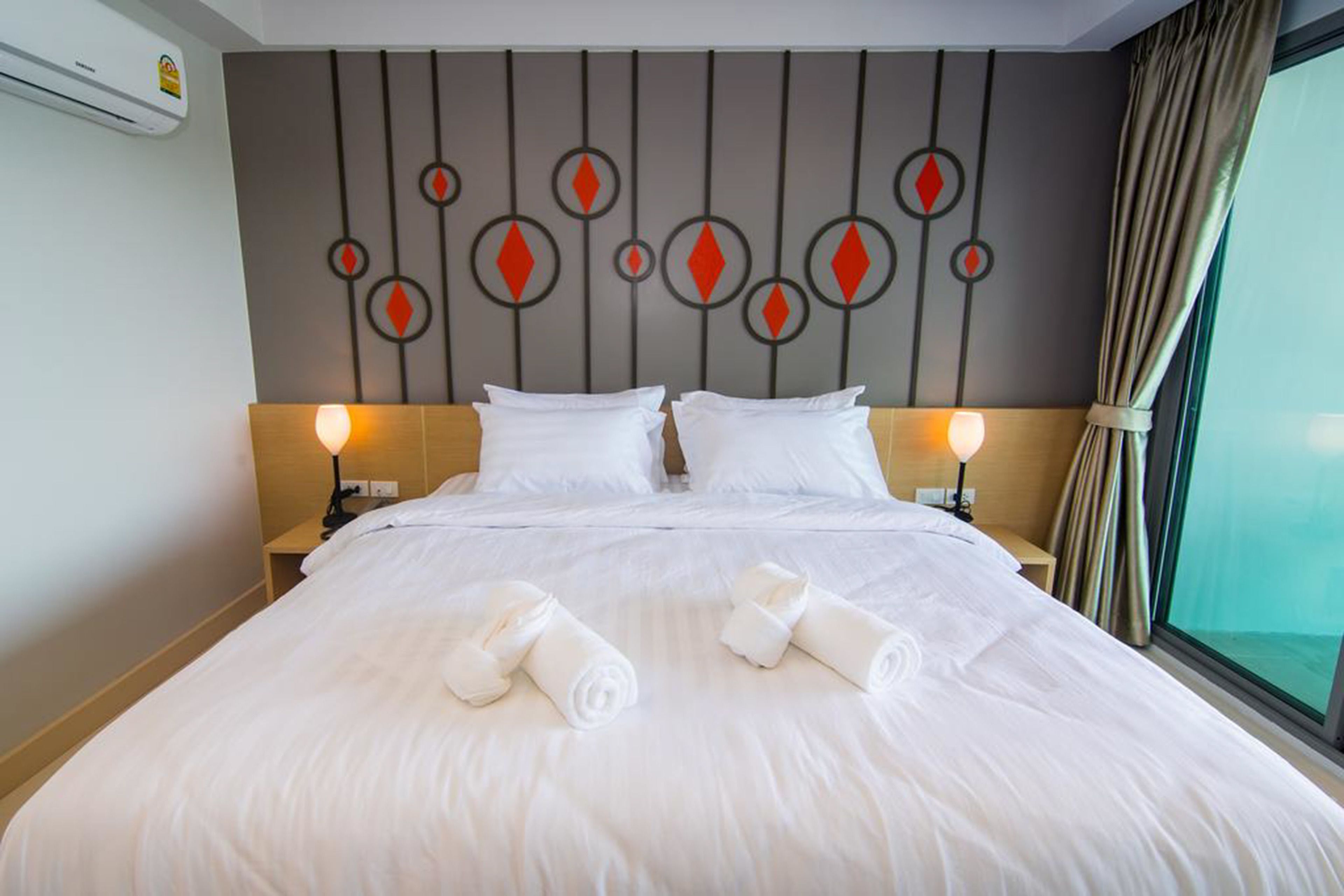 A hotel room with a large bed, two bedside tables, a decorative wall panel, and a view through a window.