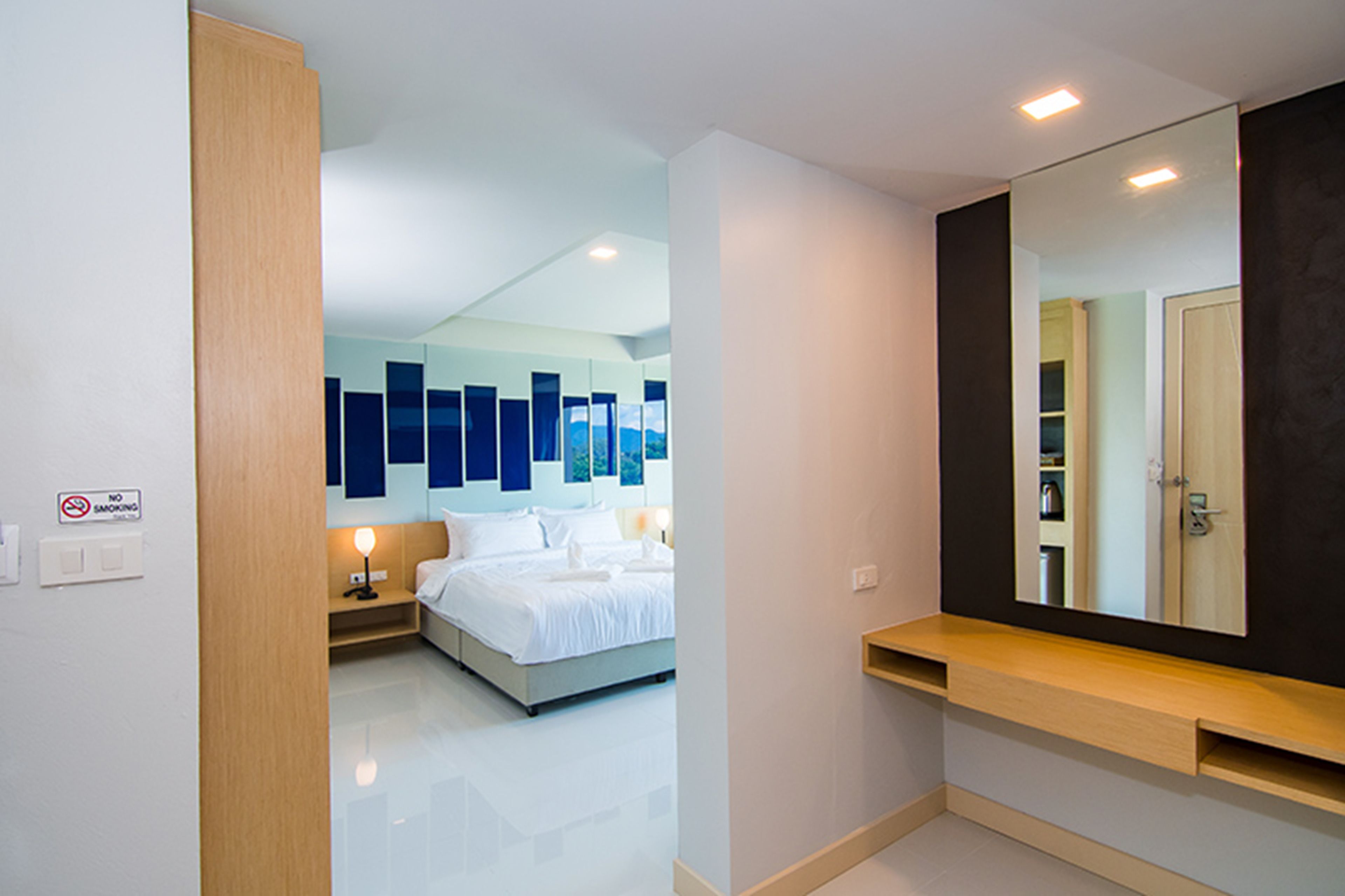 Una habitación de hotel moderna con una cama grande, una mesita de noche, un espejo y un cartel de 'No Smoking'.