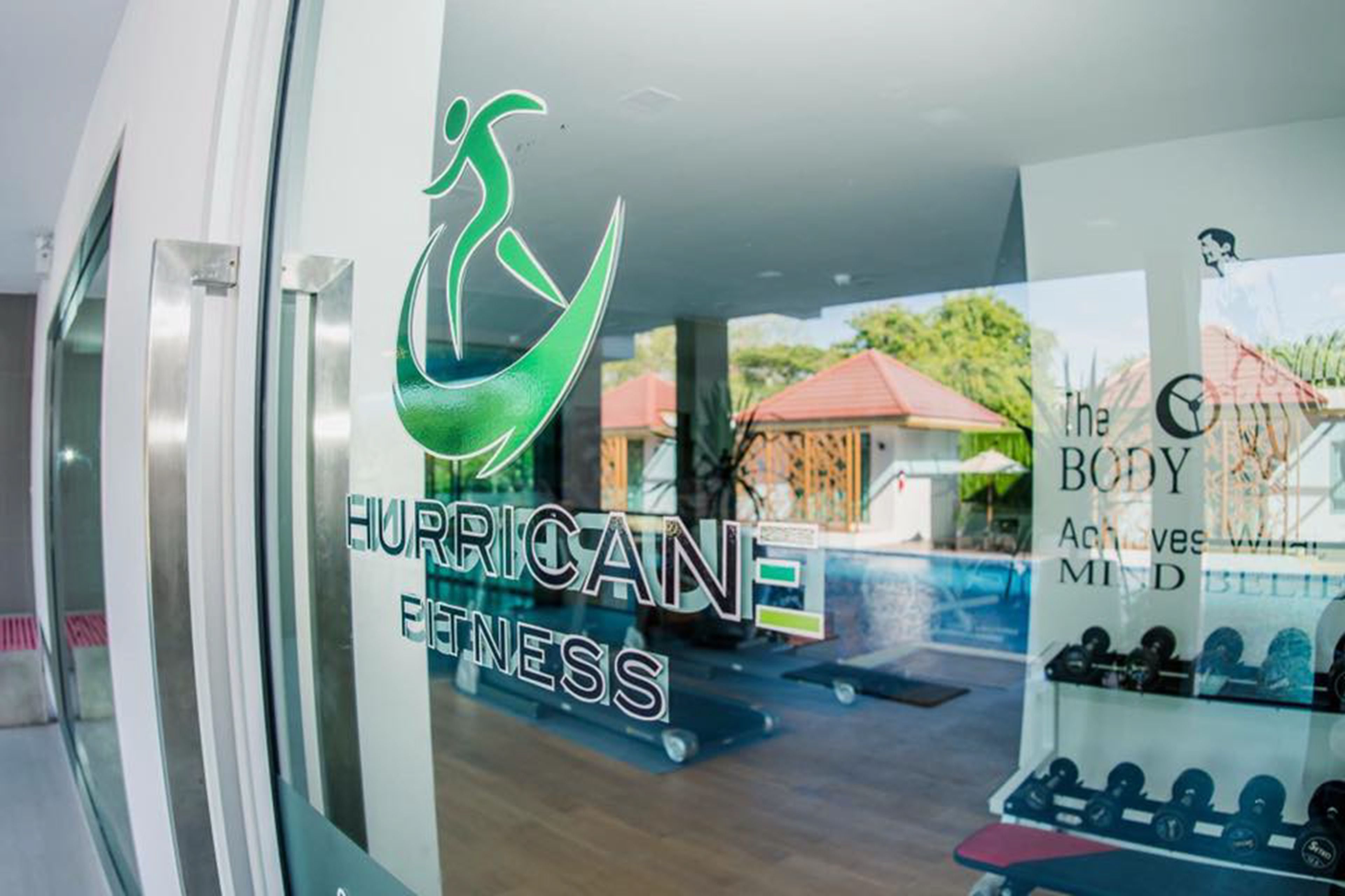A gym with a logo that reads "HURRICANE FITNESS" and a sign that says "The BODY Achieves with MIND BELIEVING".