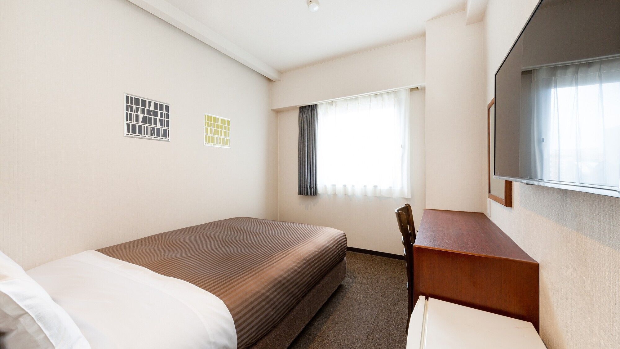 Een hotelkamer met een bed, een bureau, een stoel, een televisie en twee ramen met gordijnen.
