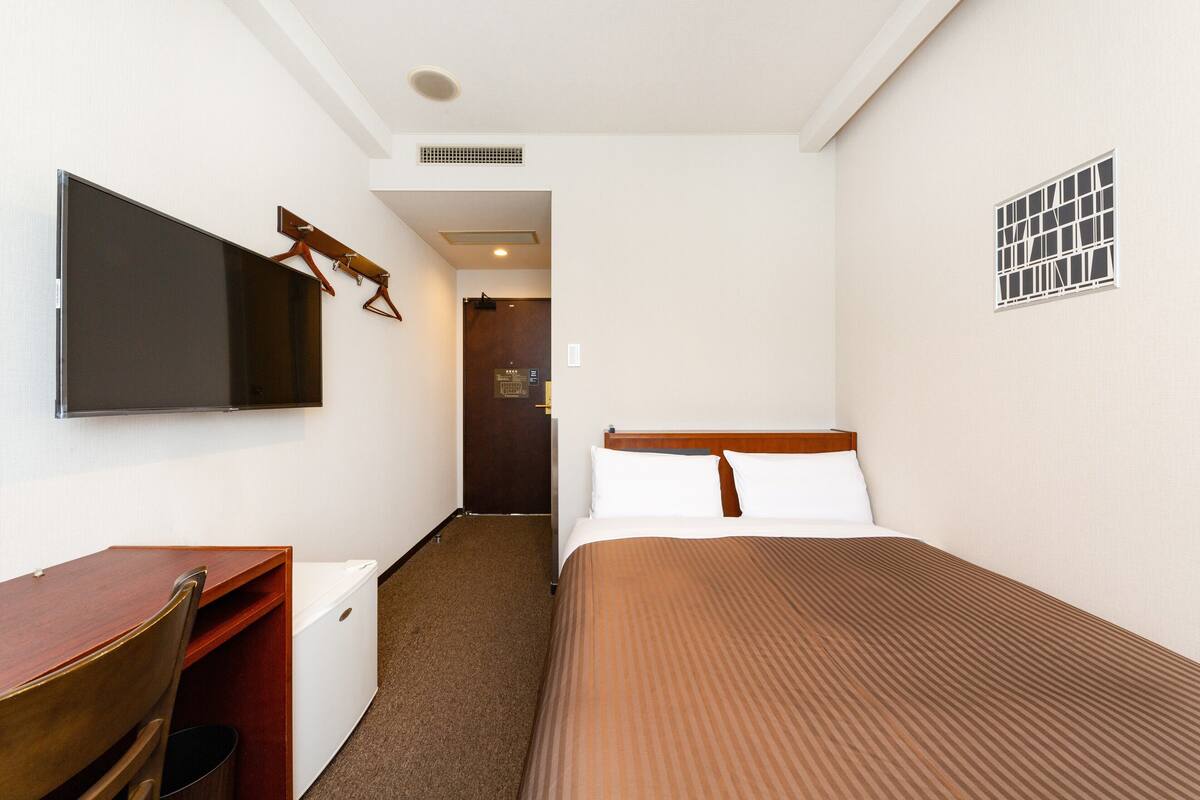 A hotel room with a bed, a desk, a chair, a television, and a door leading to another room.