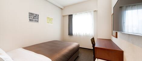 Ein Hotelzimmer mit einem Einzelbett, einem Schreibtisch, einem Stuhl, einem fenster mit Vorhängen und einem an der Wand befestigten Fernseher.