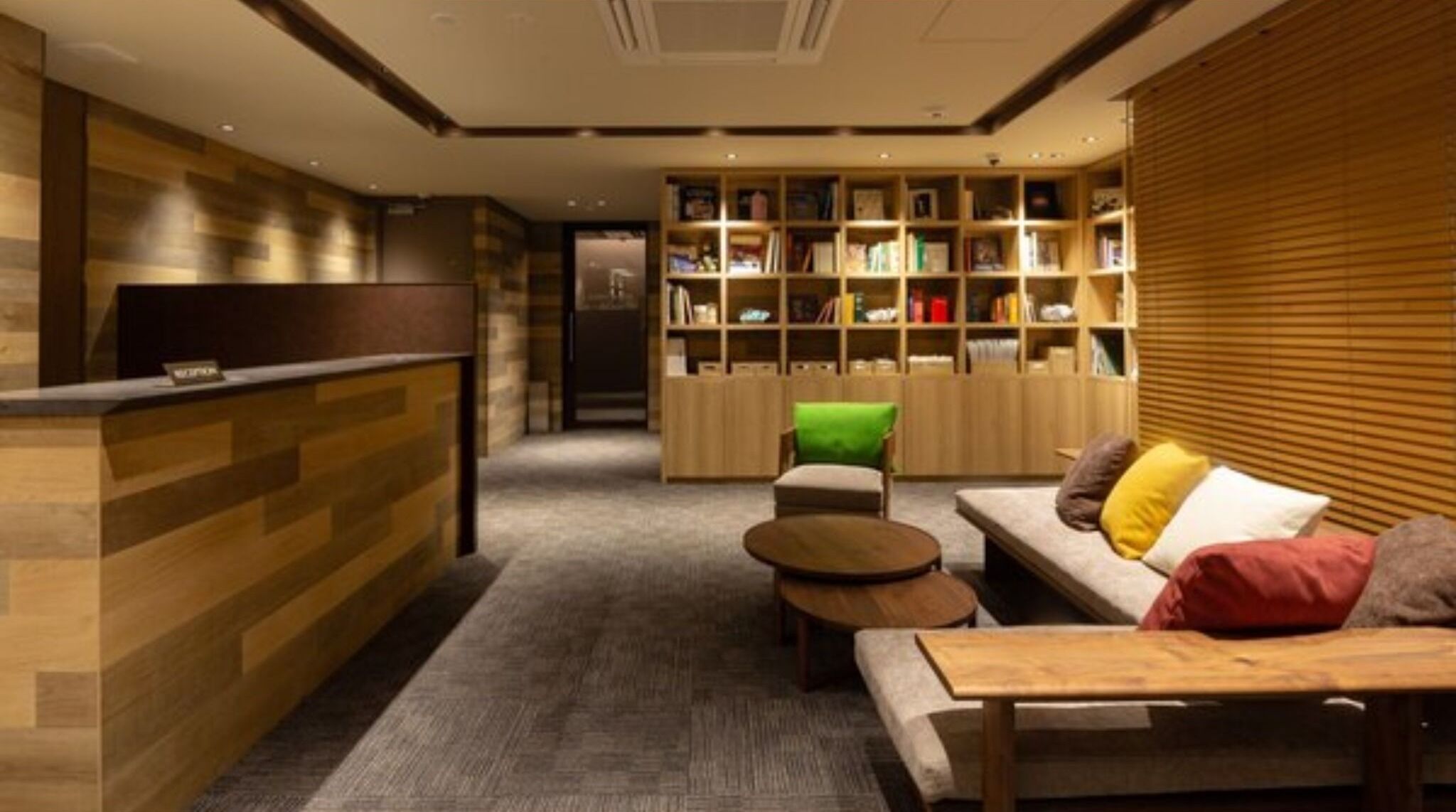 Een receptiegedeelte met een balie, een bank, een kleine tafel en een boekenplank vol boeken.