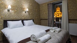 A hotel room with a large bed, two wall-mounted lamps, and a view of a cathedral through a window. - Marialuis Hotel (Tbilisi)