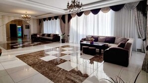 A spacious living area with a checkered floor, a chandelier, and a large window with curtains. - Marialuis Hotel (Tbilisi)