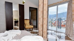 A hotel room with a bed, a chair, a large window, and a view of the city. - Marialuis Hotel (Tbilisi)