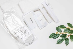 A set of toiletries including a body sponge, cotton set, comb, and toothbrush, arranged on a white surface with a green plant.
