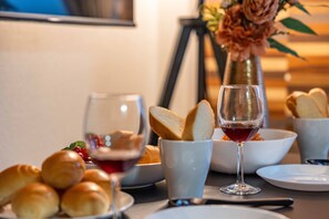A dining table with bread rolls, a glass of red wine, and a vase with flowers.