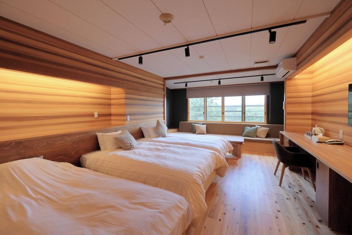 A modern bedroom with three beds, a desk, and a large window.