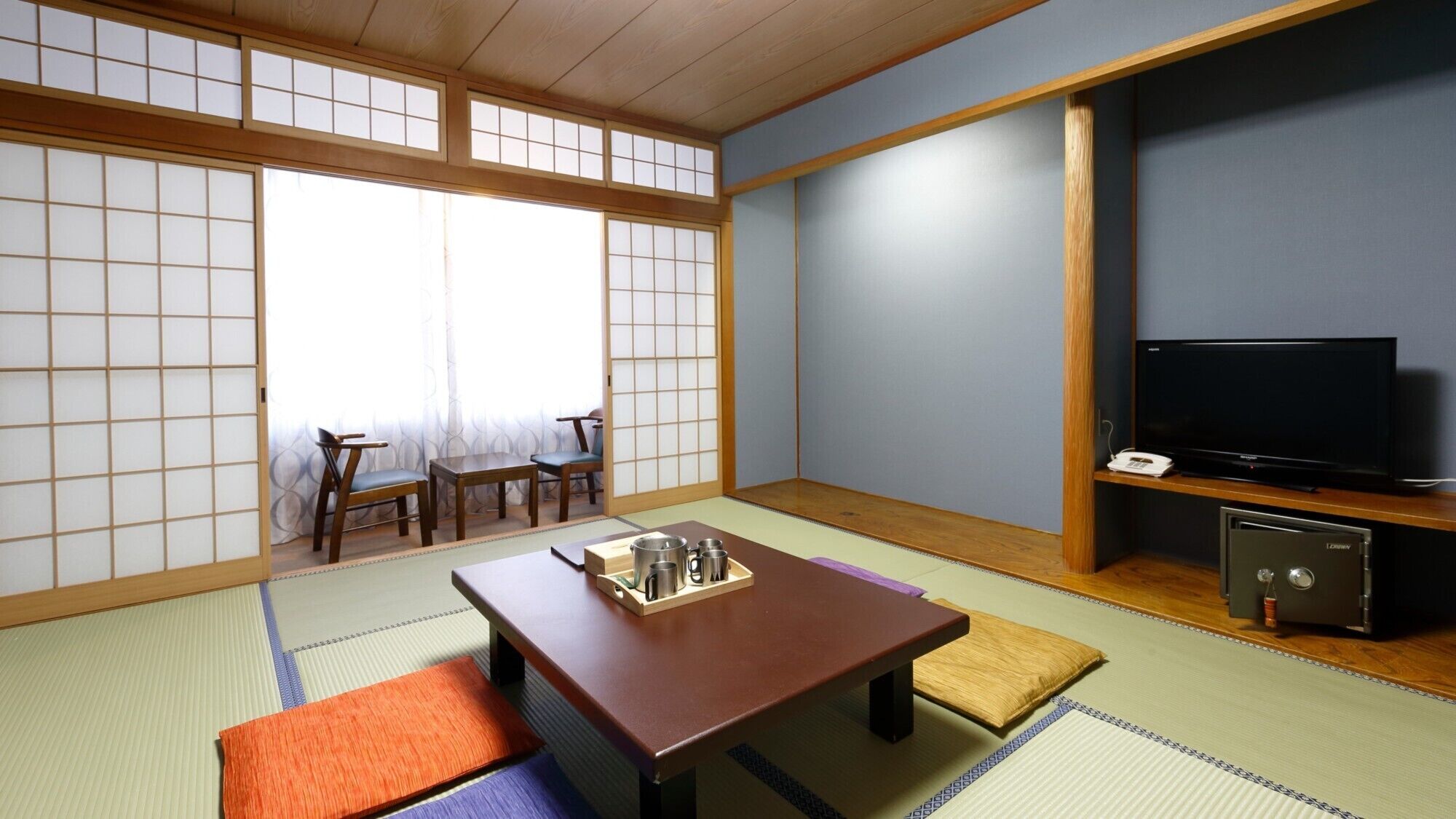 A traditional Japanese room with tatami flooring, a low table with a tray, a television, and a safe.