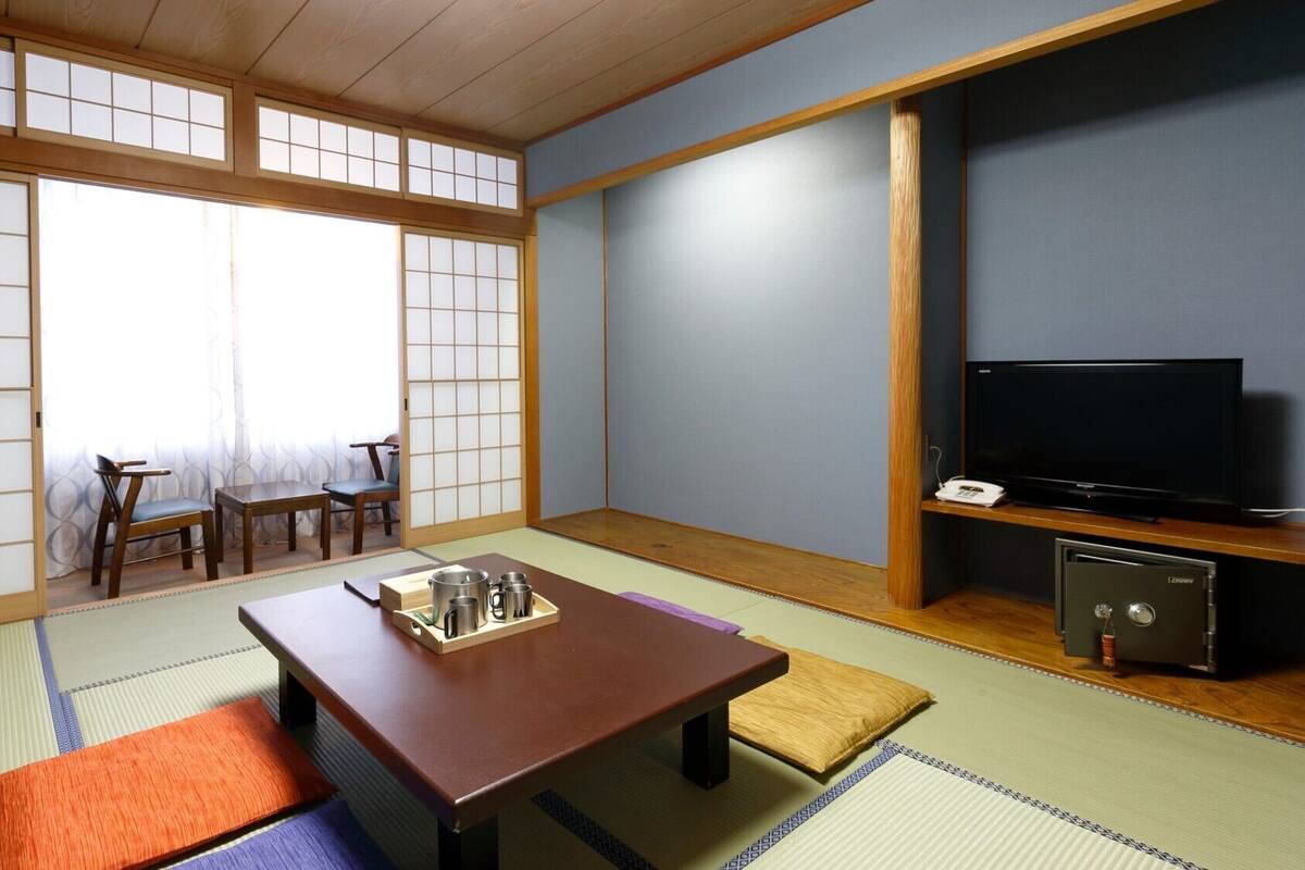 A traditional Japanese room with tatami flooring, a low table with a tray, a television, and a safe.