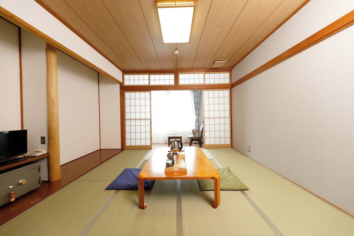 A tatami room with a low wooden table, a television, and a traditional Japanese room divider.