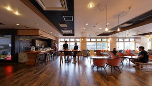 Un café amplio con suelo de madera, una zona de bar y grandes ventanales que dejan entrar luz natural.