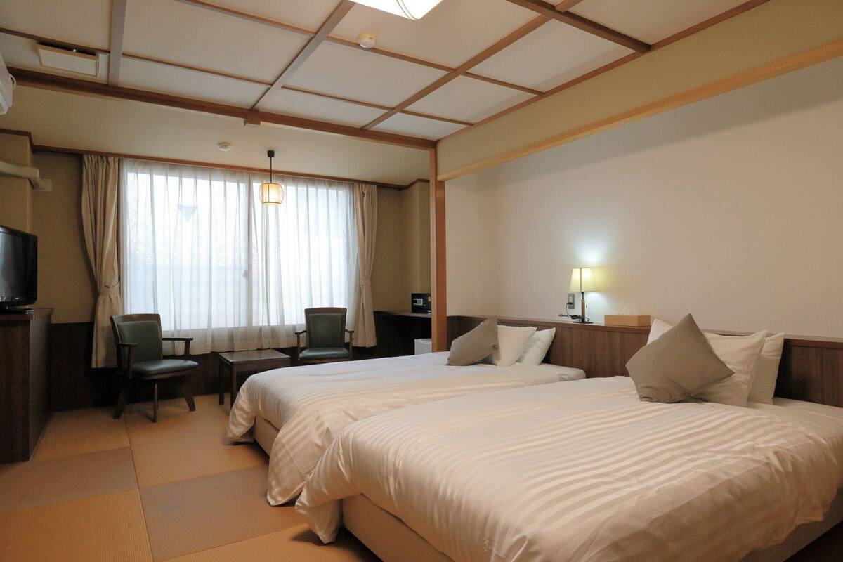 A hotel room with two beds, a desk, a chair, a television, and a window with curtains.