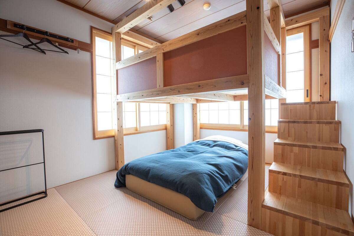 A bunk bed room with a wooden staircase, tatami mat flooring, and large windows.