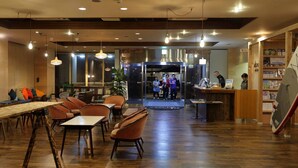 Un restaurante con suelo de madera, mesas y sillas. Hay una recepción con mostrador y una persona detrás.