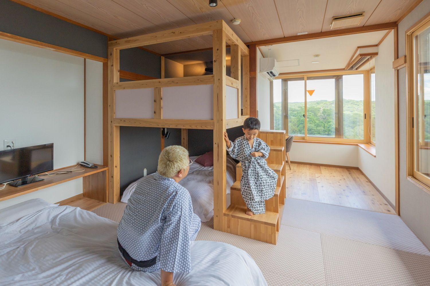 A room with a bunk bed, a television, and a large window.