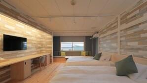 Habitación de hotel moderna con suelo de madera, un escritorio con televisor de pantalla plana, dos camas con almohadas verdes y un gran ventanal con vistas.