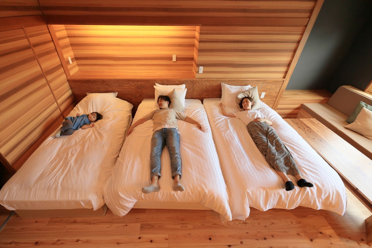 A room with three beds aligned in a row, wooden walls, and a sloped ceiling.