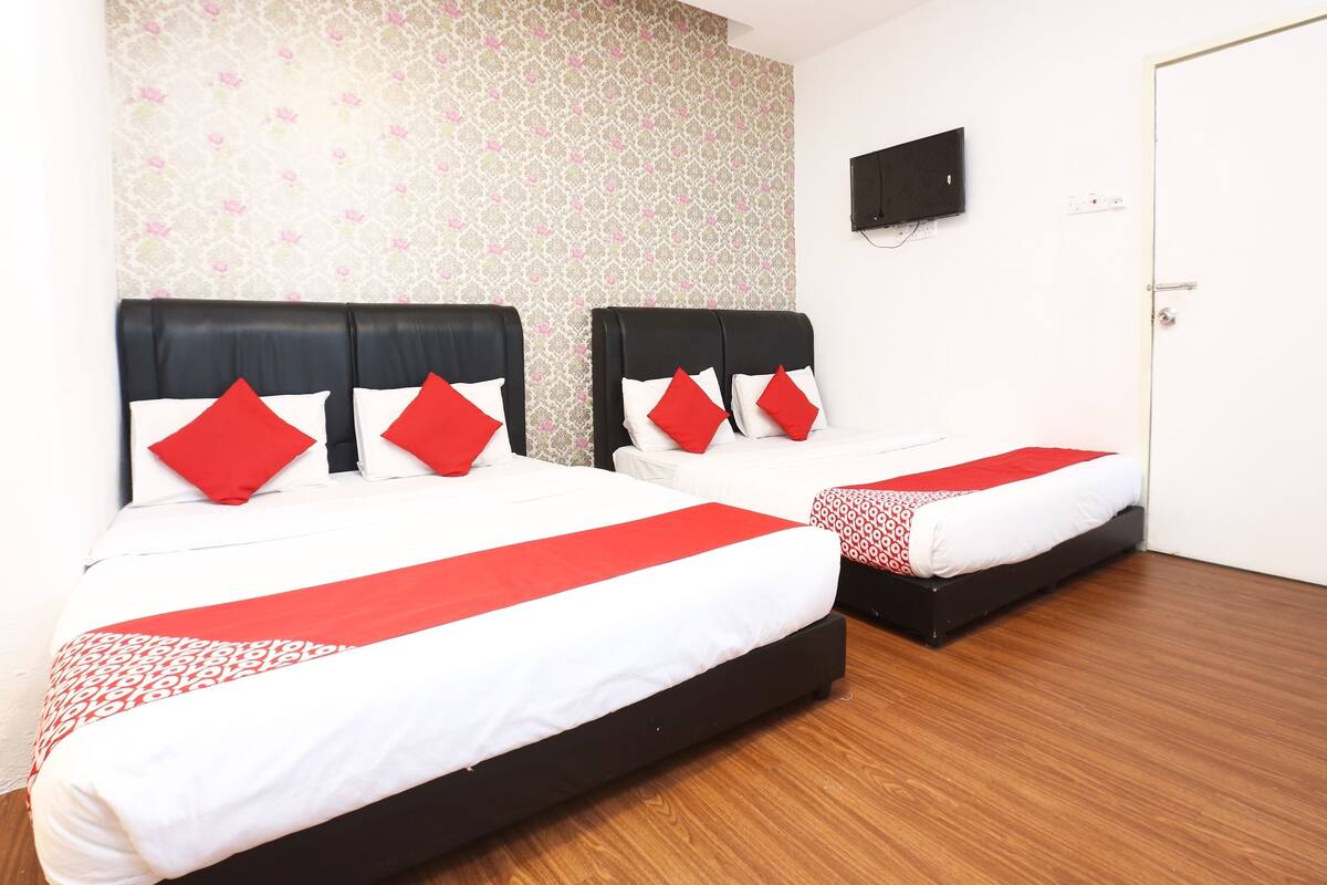 A hotel room with two beds, each with a black headboard and red pillows.
