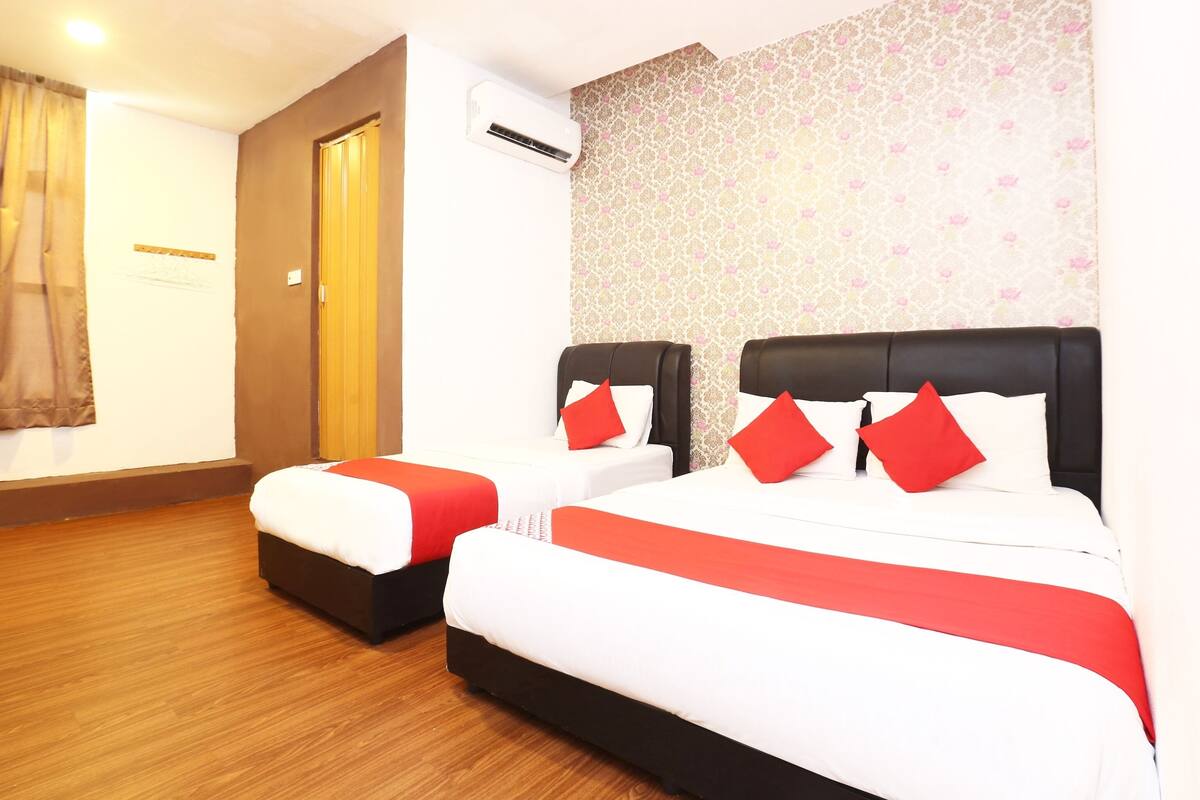 A hotel room with two beds, a wooden floor, an air conditioning unit, and a patterned wallpaper.