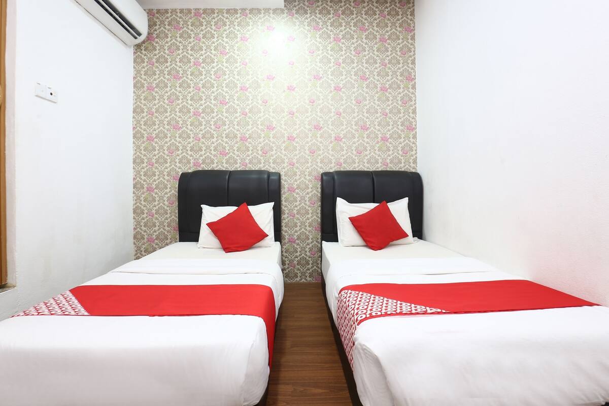 A hotel room with two beds, each with a black headboard and red pillows. The walls have a floral wallpaper pattern.