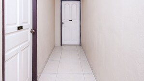 A narrow hallway with white tiled flooring and beige walls. There are two white doors, one with a black frame and the other with a white frame. - OYO 717 MR J Hotel Wakaf Che Yeh 2 (Kota Bharu)