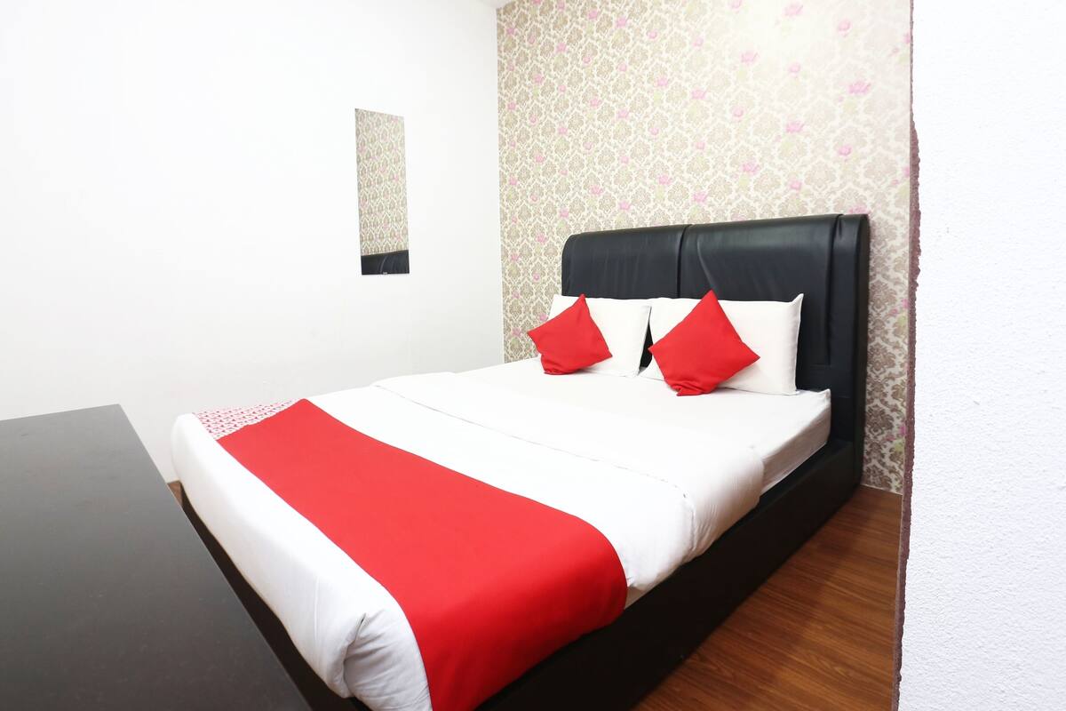 A neatly made bed with a black headboard and red and white bedding, a small window, and patterned wallpaper.