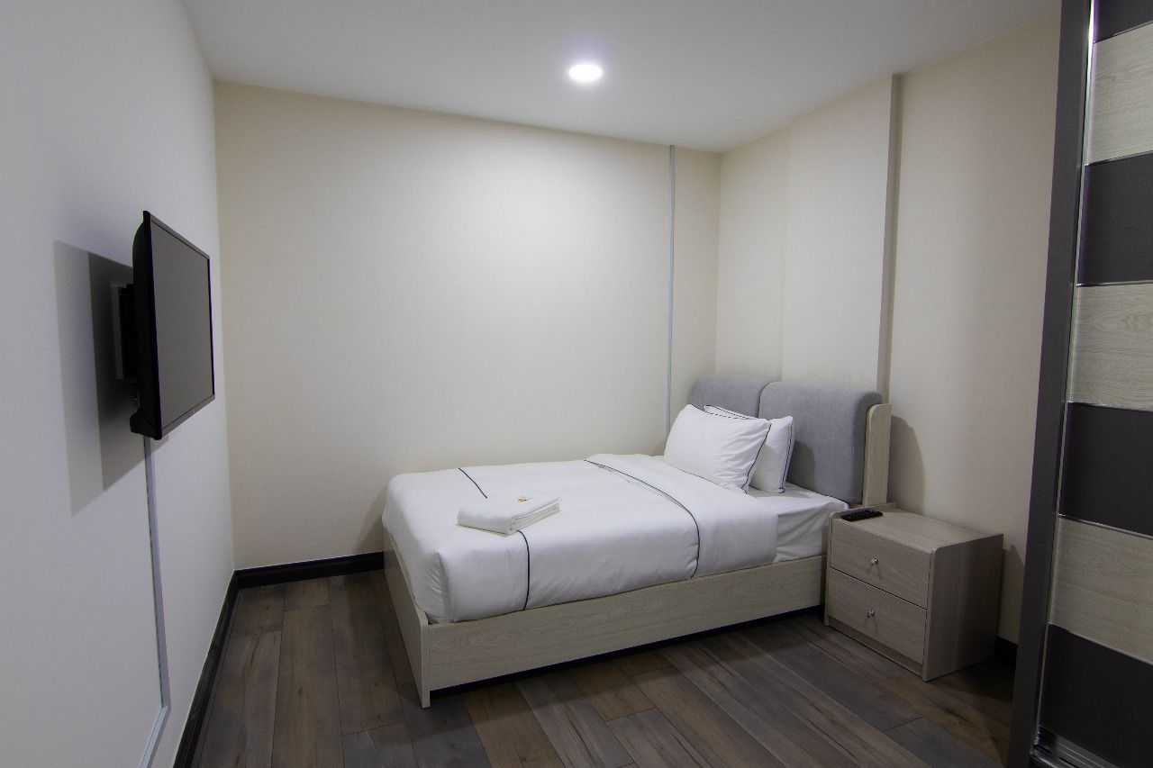 A bedroom with a bed, bedside table, and a TV mounted on the wall.